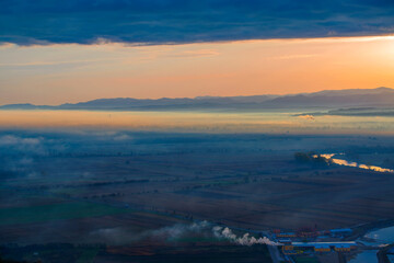 Obraz premium Aerial view of the valley in early morning mist, beautiful in the highlands. Low clouds and fog cover the sleeping meadow. Alpine mountain valley mists landscape at dawn. Serene moment in rural area