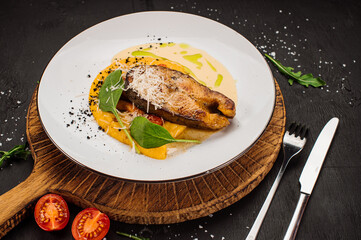 Golden white fish steak with sauce and herbs on wooden background