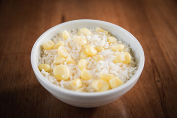 bowl of white rice with corn over a wood table.