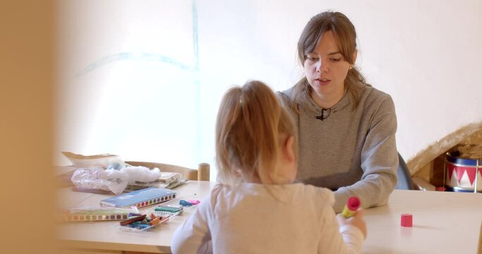 Young woman with preschool girl during therapy session at the table. Private lessons are helpful for child personal development. Peek effect, indoor lifestyle.