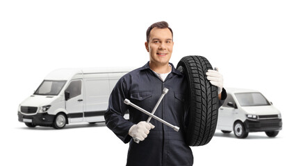 Auto mechanic posing in front of vans and holding a tire and a wrench tool