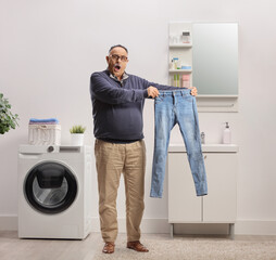 Shocked mature man holding a pair of jeans in a bathroom