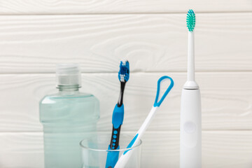 Electronic ultrasonic toothbrush, mouthwash, floss, tongue cleaner and toothpaste on white wooden background. Items for dental care and caries prevention in the bathroom. Dentistry concept. Copy space