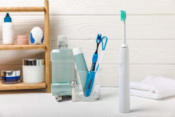 Electronic ultrasonic toothbrush, mouthwash, floss, tongue cleaner and toothpaste on white wooden...