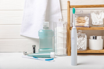 Electronic ultrasonic toothbrush, mouthwash, floss, tongue cleaner and toothpaste on white wooden...