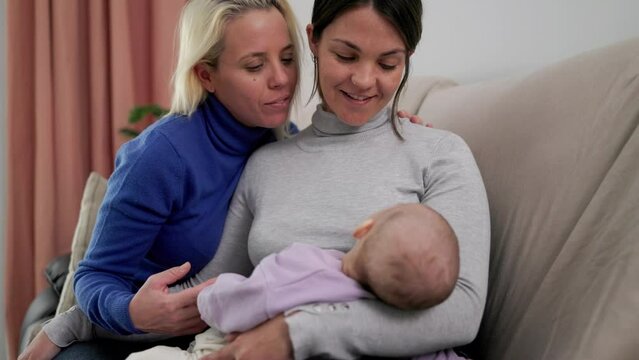 Authentic gay lesbian couple of mothers and newborn baby having tender moment at home - Lgbt family concept