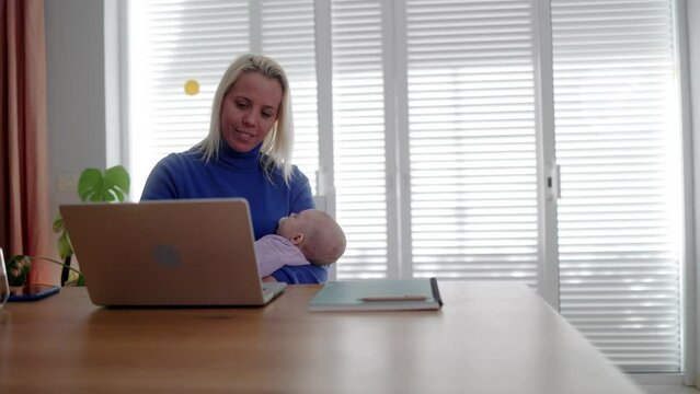 Happy business mother holding newborn infant while working on computer laptop inside home office
