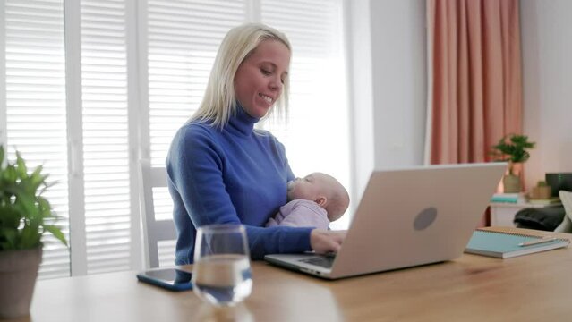 Happy business mother holding newborn infant while working on computer laptop inside home office