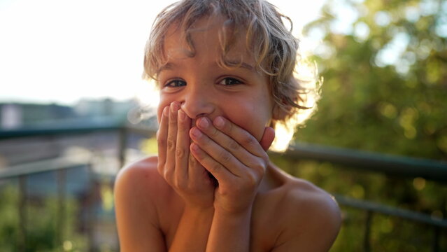 Bashful Little boy kid shocked covering mouth with hands for mistake standing outdoors. secret concept