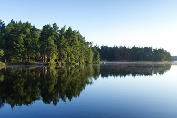 Sunny morning at a lake in Sweden with rising fog over water with forest in background