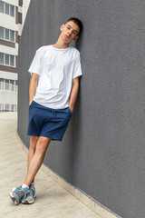 portrait of caucasian teenage boy in white T-shirt, blue shorts and sneakers on the outdoors,...