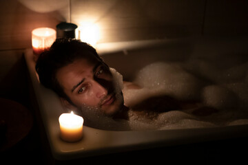 Handsome man bathing in the candlelight. Self care and spa concept