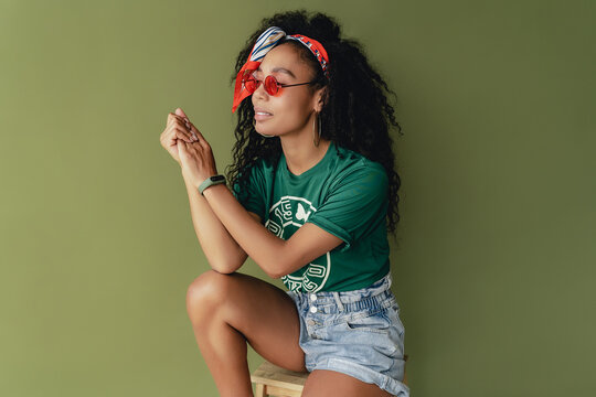 attractive black african american woman posing in stylish hipster outfit on green background