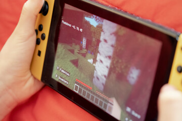 Fototapeta premium BARI, ITALY - OCTOBER 2, 2022: a kid playing with the Nintendo Switch gaming console, exploring the vast virtual world. Handheld closeup shot. 