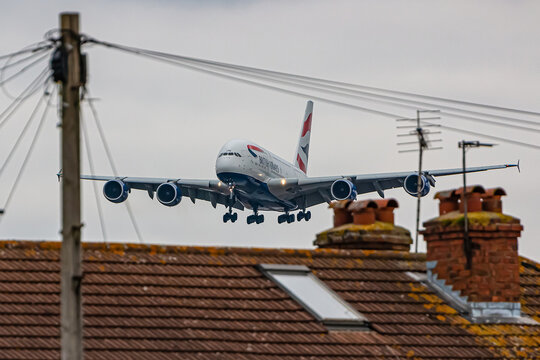 LONDON, UK - MARCH 4, 2023: Biggest passenger plane in the world, Airbus A380 British Airways approaching low above houses to London Heathrow airport.