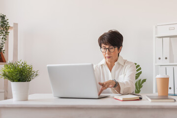 Middle-aged beautiful woman smiling while working with laptop in office, copy space and empty space for text - business and manager works concept