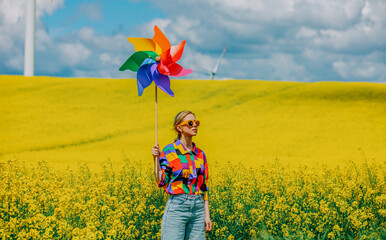 Beautiful female in 90s stylish shirt with pinwheel in rapeseed field