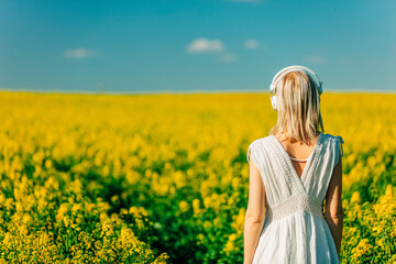 woman in dress with headphones in rapeseed field