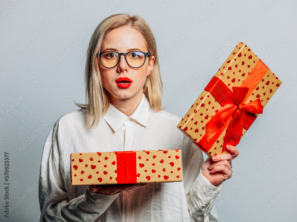 Wall mural Portrait of surprised blonde in white shirt with gift box on white background