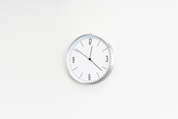 White clock hangs on the white wall. place for text, copy space.
