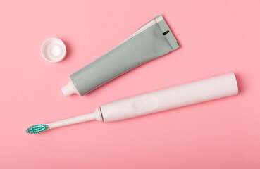 Electronic ultrasonic toothbrush and toothpaste on a pink background. Items for dental care and caries prevention in the bathroom. Dentistry concept. Copy space.