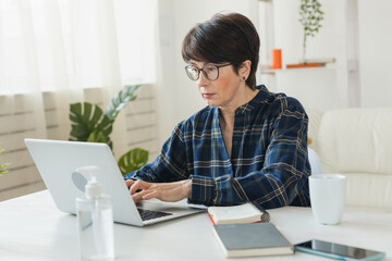 Businesswoman working on laptop computer sitting at home in pajama home wears and managing her business via home office during Coronavirus or Covid-19 quarantine