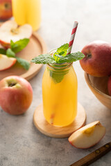 Apple juice in glass bottles, with fresh mint and red apples, wooden background. 