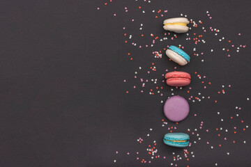 Group of coloured macaroons, column of sweets decorated with small hearts. Top view, dark background. Decoration for a candy store.