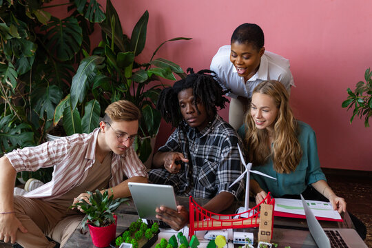 Diverse group of international students working on the urban project of modern city with renewable energy source, green areas. Concept of ecology, environment protection, waste recycling, technology