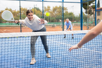 European woman serving ball while playing padel in court during training