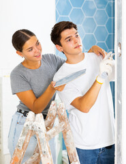Fototapeta premium Happy young couple doing repairs in the bathroom glues ceramic tiles on the wall