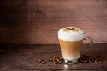 Glass cup of layered coffee drink with milk foam, wooden background and copy space