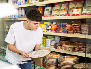 Focused young guy choosing frozen pizza for dinner during shopping at grocery store..