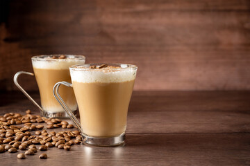 Two cups of coffee latte, with milk foam in glass cups. Coffee beans and wooden background. Copy space