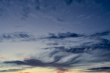 Clouds of various textures and shapes float in the sky, the sun at sunset gives golden flashes in some parts of the sky, the landscape of the evening sky