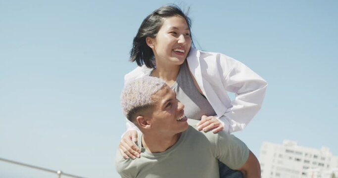 Happy biracial couple walking together and embracing on promenade, in slow motion