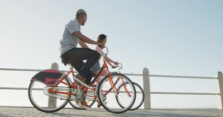 Happy biracial couple riding bikes on promenade, in slow motion - Powered by Adobe