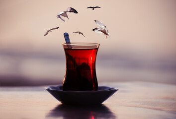 Traditional Turkish Glass of Tea. Photo Collage with Seagulls flying over a glass of tea in front...