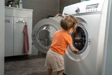 One girl small caucasian toddler child daughter standing at the washing machine in the toilet...