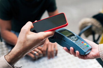 Hand of a caucasian young man approaching a smart phone to a dataphone, close up. Paying bill using NFC technology. Concept of contacless payment