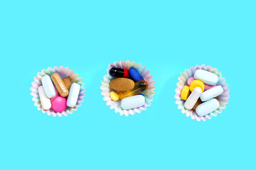 Colorful tablets with capsules and pills in cupcake wrappers on blue background.