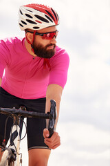 Naklejka premium Portrait of a professional cyclist in sportswear, a protective helmet and goggles in a pink jersey against the blue sky, copies. The concept of an active and healthy lifestyle.