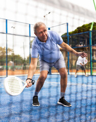 Portrait of emotional aged man enjoying friendly padel tennis match at outdoors court, view through net