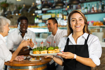 Positive female waiter holding tray with pinchos at restaurant