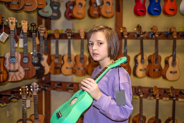 a happy child in a uklele musical instrument store, chooses a brightly colored four-string...