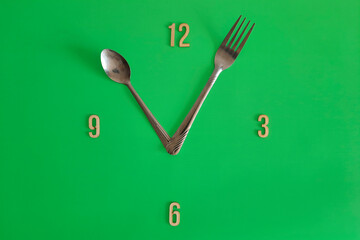 11 o'clock. Watch face with the concept of healthy eating, daily regime, diet, meal schedule. Copy space. Unusual green clock face with with spoon and fork hour hands. Flat lay. Lunch time.