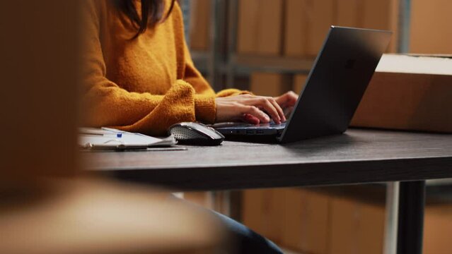 Startup owner working on stock inventory with laptop, planning order distribution for business management in storage room. Worker doing supply chain shipment at desk, retail products. Handheld shot.