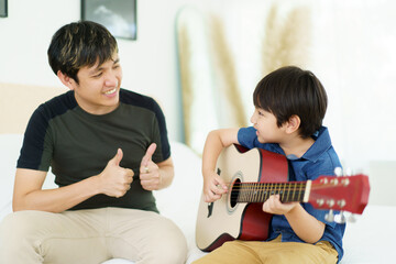 Asian little boy playing an acoustic guitar with his father, a man teaching and playing a guitar...