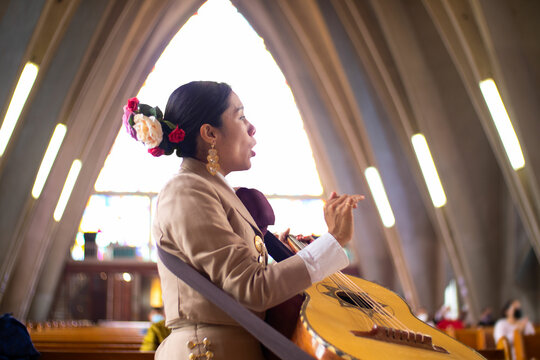 beautiful hispanic singer mariachi woman playing mexican big guitar or guitarron and singing, mexican mariachi music played in a church by women in mexico