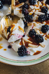 close up of Greek yogurt with honey, almonds, blackberries in white bowl with green greek key and golden spoon
